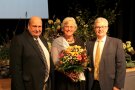 Dame mit Blumenstrauß, flankiert von zwei Herren im Anzug.