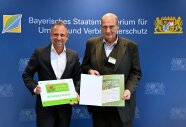 Zwei Männer im Anzug präsentieren eine Urkunde