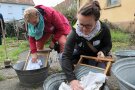 Zwei Frauen beugen sich über Metallwannen und waschen mit alten Waschbrettern.