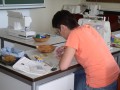 Frau mit Bleistift in der Hand über Stoff gebeugt, daneben Nähmaschinen