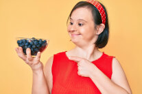 Dunkelhaarige Frau mit rotem Shirt und einem Schälchen Blaubeeren in der Hand